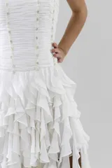 Vestido blanco de gasa con corsé drapeado y bordado con canutillos y piedras tornasoladas. Falda de volados irregulares con terminación asimétrica.