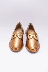 Mocasines de cuero en tono bronce metalizado, con detalle de aplique metálico dorado en el empeine y taco cuadrado bajo de madera.