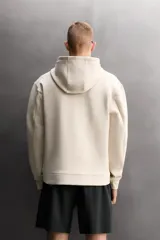 Sudadera de hombre Zara Athleticz de ajuste relajado (relaxed fit), color marrón, confeccionada en tejido técnico compacto con mezcla de algodón y elasticidad. Cuenta con cuello con capucha ajustable con cordones negros, manga larga, bolsillo frontal tipo canguro con un pequeño bolsillo termofijado con cierre, y acabados con rib en puños y cintura.