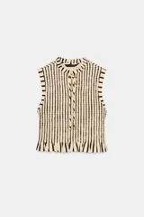 Top sin mangas de cuello redondo con lazo frontal, confeccionado en tejido con textura de nido de abeja elástico y estampado de rayas verticales. Presenta terminaciones con volantes en el ruedo.