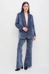 Blazer de terciopelo azul con solapas anchas y cierre frontal de un botón. Presenta un diseño entallado de manga larga con textura suave y acabado ligeramente brillante.