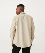 Camisa de corte regular, color beige, con cuello camisero, mangas largas, cierre frontal con botones y dos bolsillos con solapa en el pecho.
