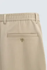 Pantalón de corte recto confeccionado en tejido elástico, con cintura elástica, pliegues frontales, bolsillos laterales y bolsillos traseros de vivo con botón.