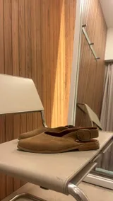 Sandalia chata color marrón con textura tejida, punta fina y tira trasera con hebilla dorada.