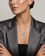 Collar de acero con cadena fina que presenta pequeños apliques de circonias a lo largo de su extensión. El dije central tiene un diseño circular doble, con el borde exterior pavé de circonias y tres pequeñas piedras rojas incrustadas en la parte inferior del círculo interior.