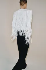 Chaqueta de cuello redondo y manga larga con hombreras, completamente cubierta de flecos con lentejuelas. Cuenta con forro interior y cierre frontal.