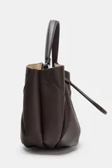 Bolso de mano tipo saco mini, color marrón oscuro, con detalle de pespuntes en el cuerpo y cierre mediante botón imantado. Incluye tira ajustable frontal y compartimento interior con cremallera.