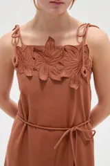 Vestido largo de algodón color blanco, con tirantes finos ajustables con lazos en los hombros, escote recto decorado con apliques florales tridimensionales, cordón ajustable en la cintura y falda larga con volados horizontales.