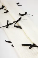 Calentadores de punto color crema con detalle de lazos negros.