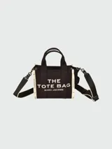 Bolso tipo tote de Marc Jacobs, confeccionado en tejido jacquard negro con detalles en color crema. Presenta el nombre del modelo estampado en el frente, doble asa superior y correa ajustable extraíble.