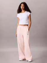 Pantalón de felpa francesa rosa pastel, de corte holgado con basta ancha y tiro medio. Posee cintura elástica, bolsillos laterales y una pequeña insignia blanca con el logotipo de Calvin Klein en el lateral izquierdo.