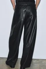Pantalón de tiro medio confeccionado en tejido efecto piel. Presenta un diseño de pierna ancha tipo balloon, cintura con trabillas, cierre frontal con cremallera y botón, y cinco bolsillos.