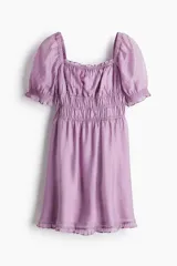 Vestido corto color lila con escote cuadrado, cuerpo fruncido elástico bajo el busto, mangas cortas abullonadas con volados y falda con leve vuelo.