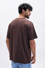 Remera de manga corta color marrón oscuro, corte oversize, con cuello redondo y estampado frontal con el texto "UNIVERSAL FUTURE" en color crema.