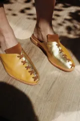 Mules (zapatos destalonados) de cuero, combinando color amarillo mostaza y dorado metálico, con detalle de cordones cruzados en la puntera.
