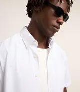 Camisa blanca con rayas celestes, de corte clásico, manga corta y cuello solapa. Confeccionada en fibra de bambú y poliéster.