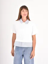 Remera de manga corta color blanco con cuello camisero y detalle de bajo en tela rayada azul y blanca, simulando una camisa debajo.
