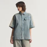 Camisa de jean de manga corta Adidas, confeccionada en 100% algodón, con diseño inspirado en la ropa de trabajo, cierre frontal con broches a presión, cuello camisero, un bolsillo en el pecho con solapa y las clásicas tres tiras de la marca en las mangas.