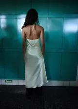 Vestido midi de tejido satinado en color beige claro, con escote halter en pico, detalles fruncidos en el pecho, tirantes finos y abertura lateral.