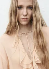 Blusa de viscosa color beige, con diseño de volantes frontales, cuello escotado con cierre de lazo y mangas largas acampanadas con volantes en los puños.