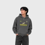 Hoodie gris de corte holgado con capucha, confeccionado en algodón premium. Presenta un estampado gráfico frontal con el logo y nombre de la marca en tonos amarillos y crema.