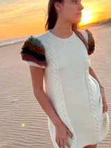 Vestido midi de punto color marfil, confeccionado en lana merino, con mangas cortas decoradas con flecos mullidos de varios colores y trenzas verticales al frente.