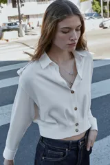 Camisa corta de cuello solapa y manga larga, con trabillas decorativas en los hombros. Presenta pliegues delanteros, elástico en la espalda y cierre frontal con botones.
