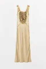 Vestido largo color beige de viscosa, con escote cuadrado, tirantes anchos, detalles drapeados, volantes y aplicaciones de encaje a contraste en el pecho. Cuenta con cierre trasero de botones.