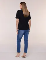 Blusa holgada de color negro, con escote redondo y mangas cortas adornadas con apliques de tachas metálicas. Presenta delicadas tablas centrales en el frente y un diseño elegante.