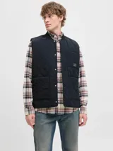 Chaleco acolchado negro con diseño de costuras onduladas, cuello estilo baseball y cierre frontal con botones a presión. Cuenta con dos bolsillos frontales de parche y un bolsillo pequeño en el pecho con etiqueta de marca.