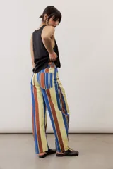 Pantalón de corte ancho y relajado con rayas verticales multicolor en tonos azul, marrón, amarillo, blanco y negro.