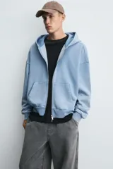 Sudadera con capucha y cierre de cremallera, de corte relajado (relaxed fit), confeccionada en algodón con interior afelpado. Presenta bolsillos frontales tipo canguro y acabados en rib. El tejido tiene un efecto lavado que le da un color negro desgastado.