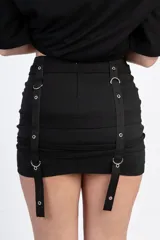 Minifalda negra con tres hileras de correas ajustables con hebillas plateadas.