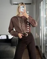 Camisa de manga larga color blanco con bordados geométricos en negro a lo largo de la botonadura frontal y en los puños. Presenta cuello mao y cierre frontal con botones.