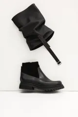 Bota corta de cuero color marrón claro (visón) con caña arrugada y suela track negra gruesa. Presenta un detalle de tira de cuero con hebilla en el tobillo.