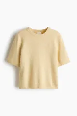 Remera corta de punto suave color amarillo, de manga corta, con cuello redondo y terminaciones acanaladas.