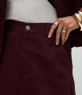 Pollera evasé de sarga color bordó, con cintura alta, presillas para cinturón, cierre frontal con botón y cremallera, y largo midi.
