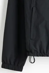 Campera rompevientos negra de nylon repelente al agua, con capucha ajustable, cierre frontal, bolsillos laterales y puños elásticos.