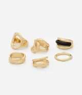 Kit de seis anillos de diseño variado con acabado en tono dorado claro. Incluye piezas de metal con texturas lisas, torcidas y caladas, además de un anillo con detalle de resina negra. Diseñados para ser usados en conjunto o por separado.