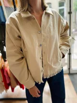 Campera color beige de gabardina con corte clásico, cierre frontal con botones y ruedo con flecos.