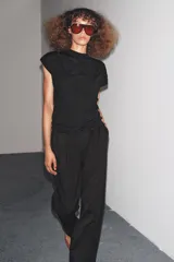 Top negro de manga corta y cuello subido, con detalle de nudos y frunces distribuidos en el frente y laterales, creando textura.