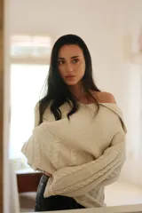 Buzo de tejido de punto color crudo, con cuello amplio que puede usarse caído sobre los hombros, mangas largas con trenzas de ochos y cuerpo con punto arroz.