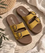 Sandalias planas de mujer con doble tira en tono mostaza de acabado gamuzado, sujetas por dos hebillas metálicas de estilo rústico y base marrón.