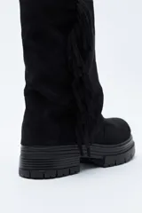 Bota de caña media con flecos laterales, confeccionada en material con textura tipo gamuza. Presenta una silueta relajada y suela robusta con base dentada.
