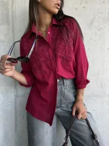 Camisa de color bordó con cuello clásico y cierre frontal de botones. Presenta un diseño distintivo con paneles de encaje bordado en la parte superior delantera, mangas largas con puños y un corte recto.