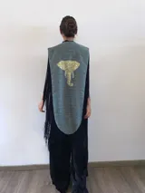 Poncho estructurado color celeste con bordado de elefante en la espalda. Presenta un diseño asimétrico, más corto adelante y largo atrás, con flecos negros que rodean toda la prenda.
