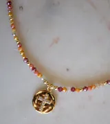 Collar de cristales facetados en tonos naranja, rojo y beige, con esferas doradas intercaladas. Incluye un dije redondo de baño de oro con una cruz de circonitas incrustadas.