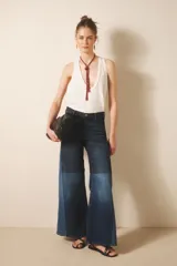 Jean de tiro alto con pierna palazzo, ajustado en cintura y caderas, con recortes a contratono en el lateral y a media pierna que generan un vuelo pronunciado. Confeccionado en tejido de elastano, incluye cierre y botón, y forrería de bolsillos estampada con el logo de la marca.