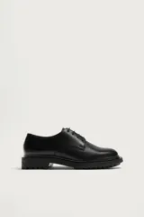 Zapato de vestir tipo derby fabricado en piel color negro, con horma redonda y suela track dentada.