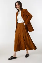 Falda midi de gamuza color marrón, con diseño de corte amplio, tajo lateral y cintura con elástico en la parte trasera. Cuenta con cierre metálico lateral y forro interior.